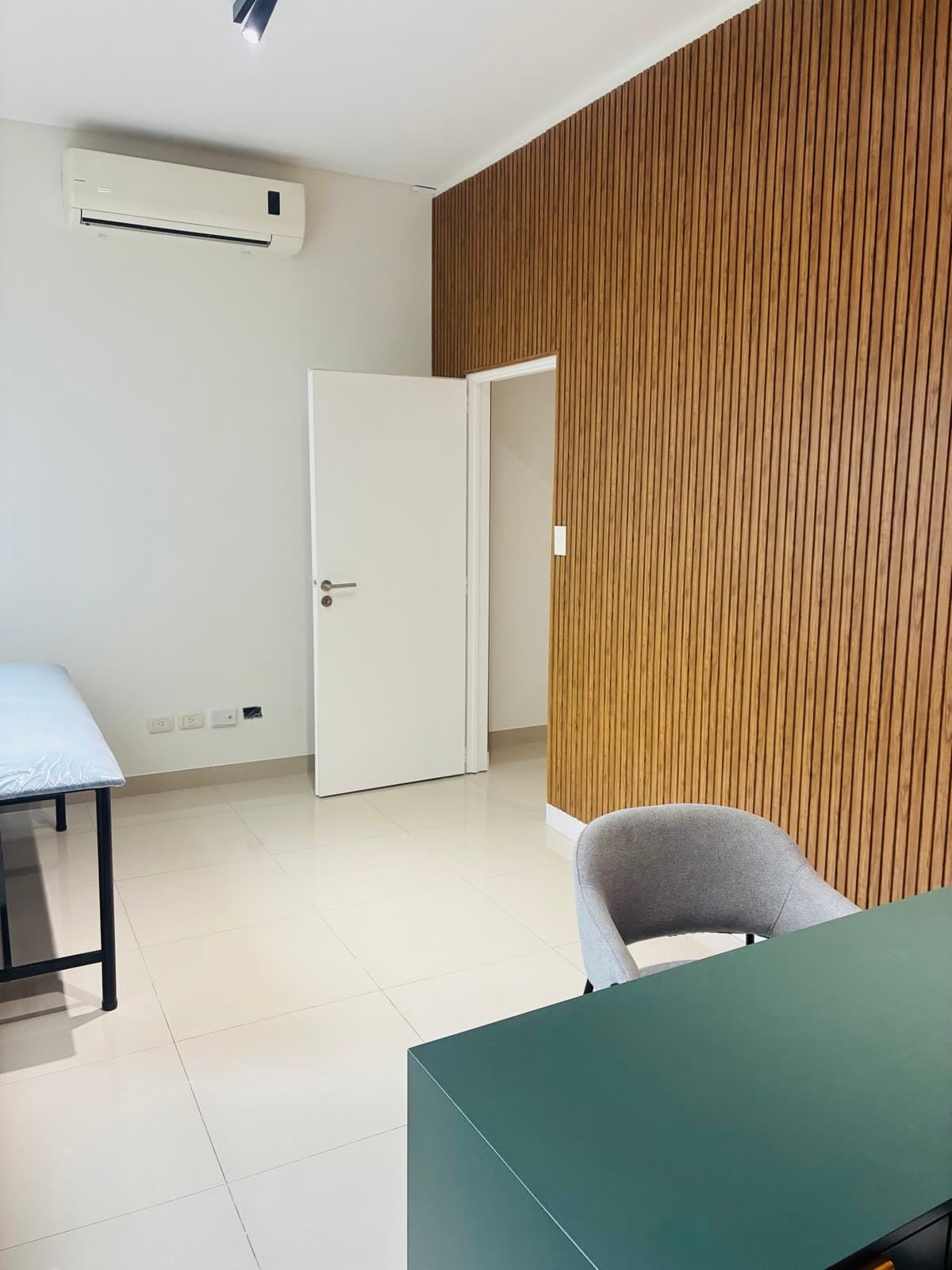 Consultorio 2: escritorio, silla de paciente, camilla y pared de listones de madera