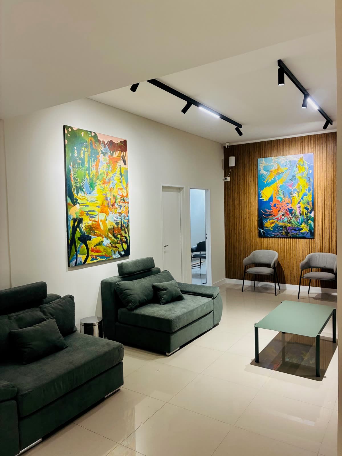 Sala de espera del centro médico con sillones verdes, mesa baja y cuadros sobre pared de madera