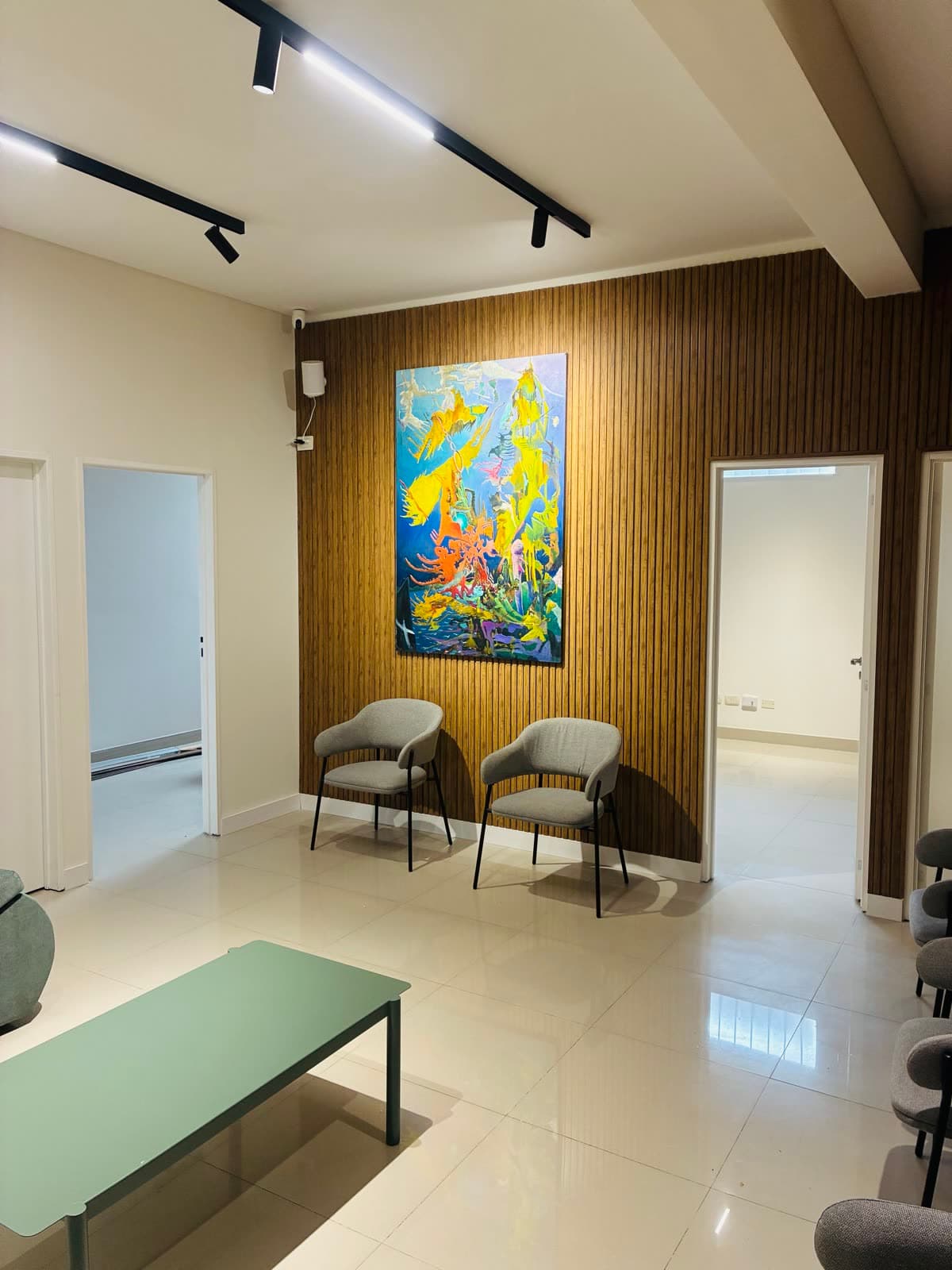 Sillas de espera frente a una obra de arte colorida sobre pared de listones de madera