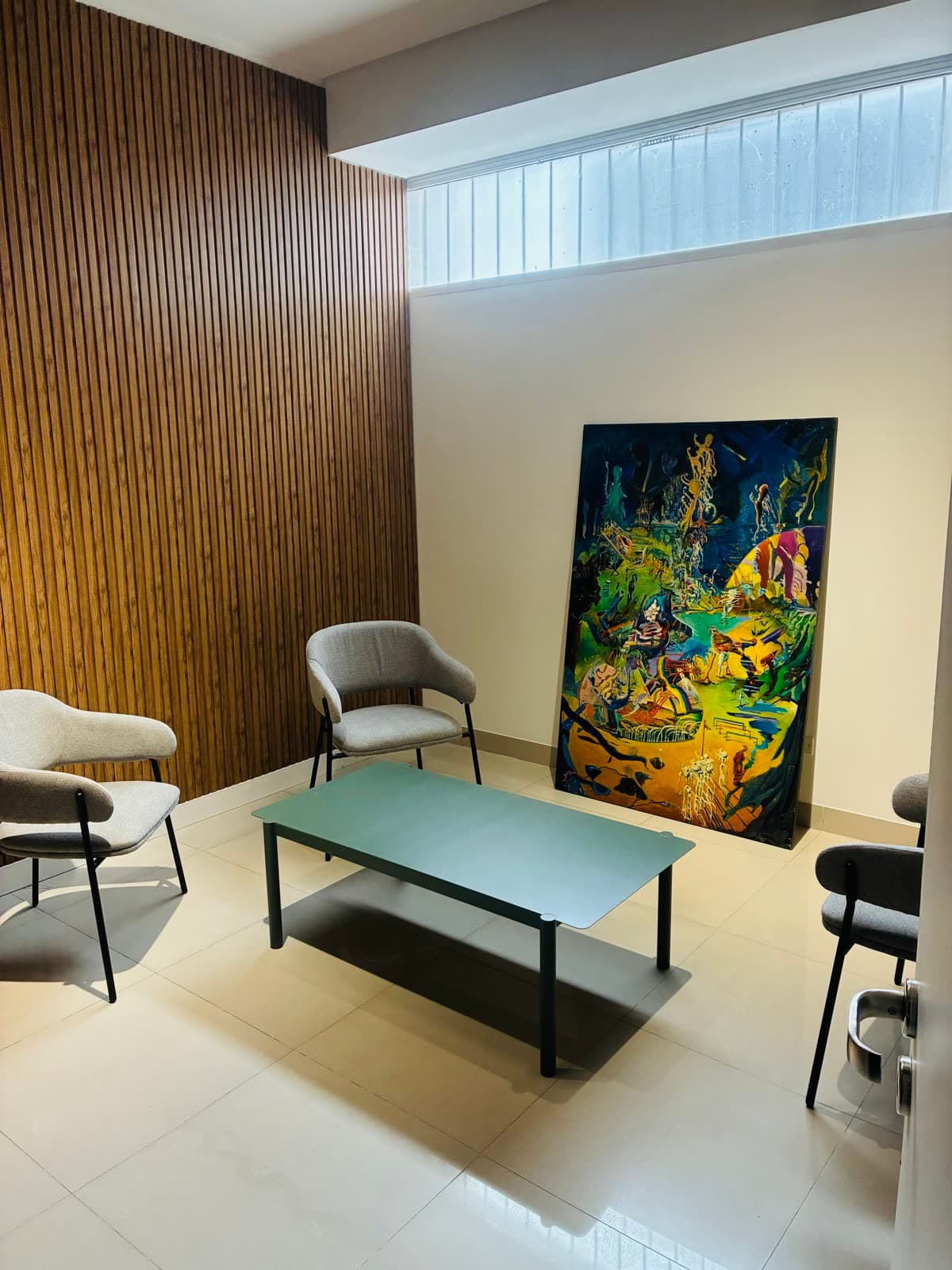 Sala de espera privada con sillones, mesa baja verde y obra de arte apoyada en la pared